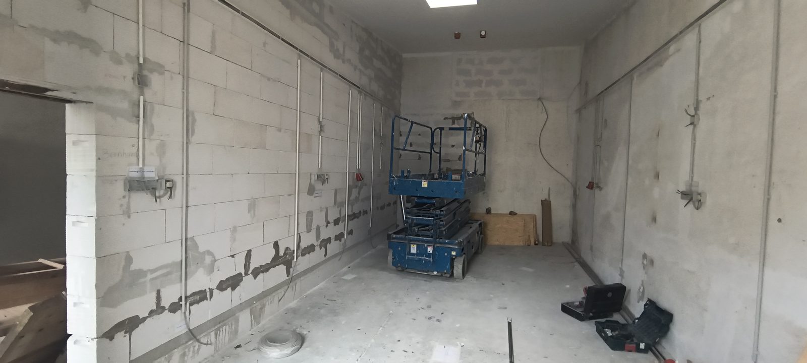 Der leere Werkstattraum: Kalksandsteinwände mit frisch verlegten Leerrohren und Schlitzen, eine Hebebühne in der Mitte, Werkzeugkoffer auf dem Estrich.